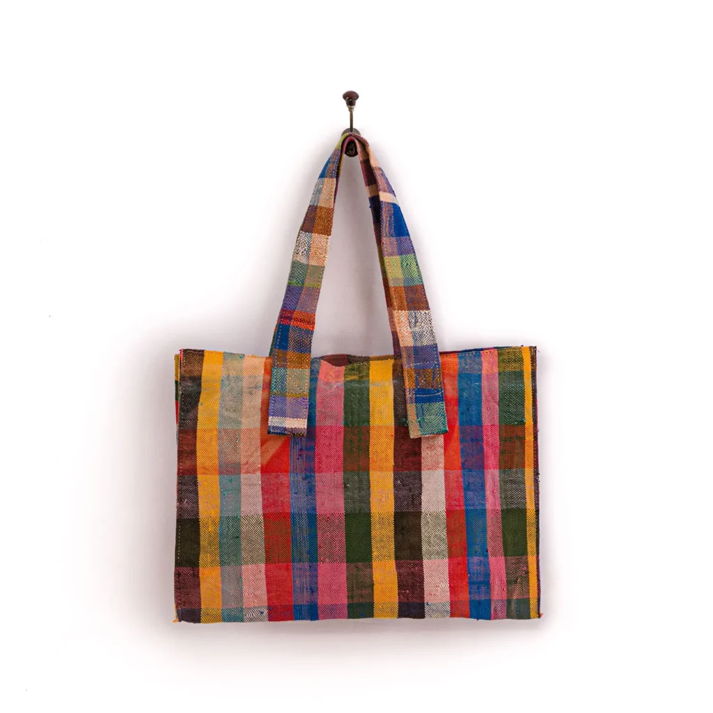 Colorful checked tote bag with various shades of orange, blue, green, and pink, hanging on a hook against a white background.