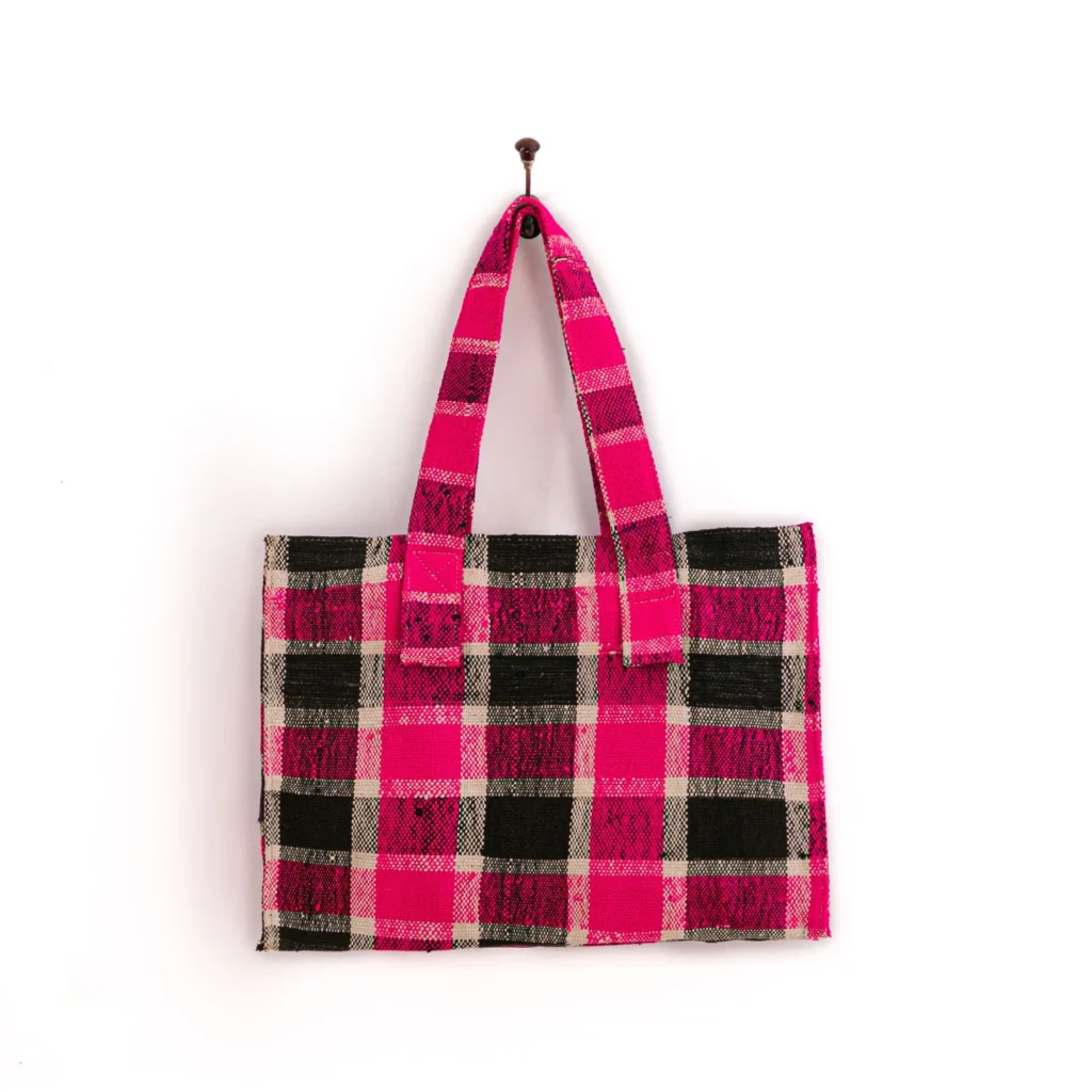 An upcycled weekend bag with a pink, black, and beige checkered pattern hangs on a nail against a white wall.