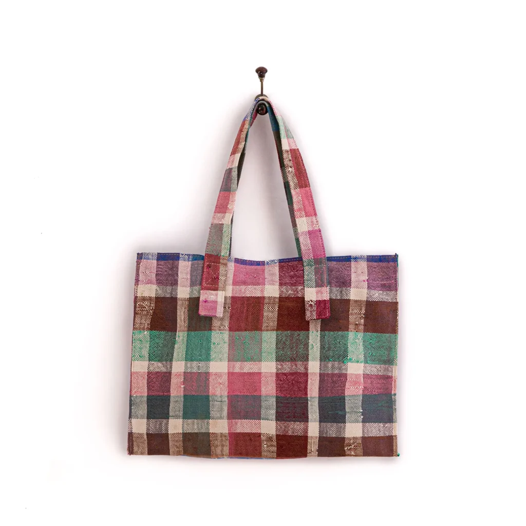 Plaid tote bag in shades of pink, green, and brown with two handles, hanging on a wall hook.