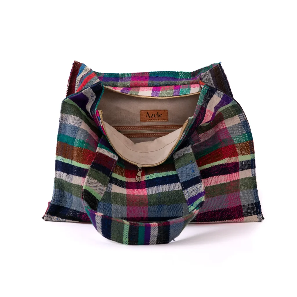 Multicolored plaid fabric tote bag open to reveal beige interior and a label reading Azele inside.