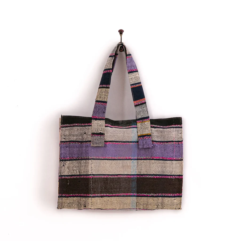 A multicolored striped fabric tote bag hanging on a wall hook.