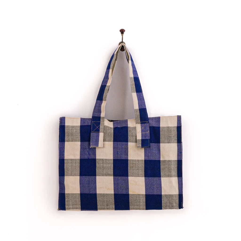 A blue, gray, and white checkered tote bag hangs on a wall hook against a white background.