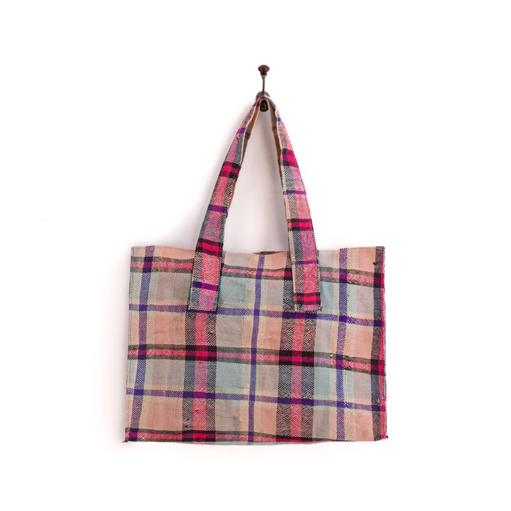A multicolored plaid tote bag with pink, blue, and beige hues hangs on a hook.