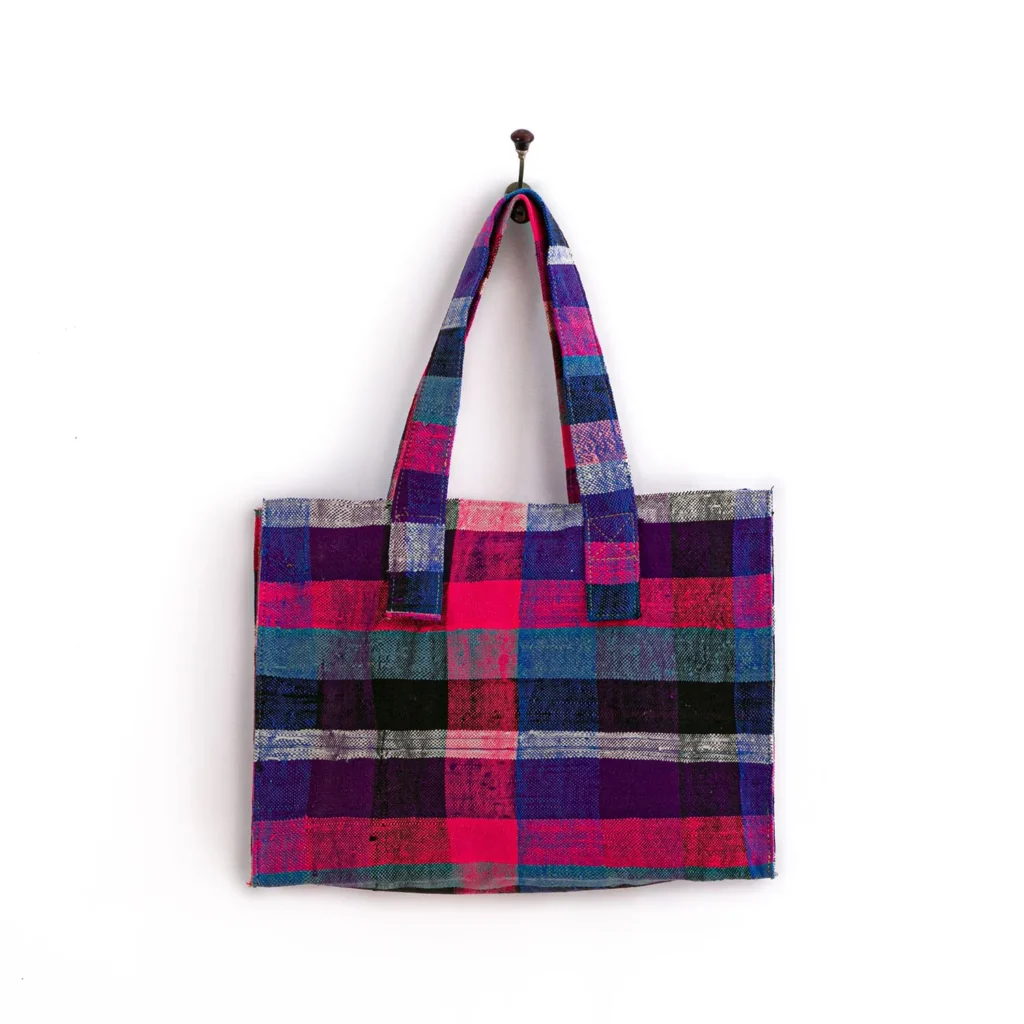 Tote bag with a plaid pattern in shades of pink, purple, black, and gray, hanging on a wall hook.