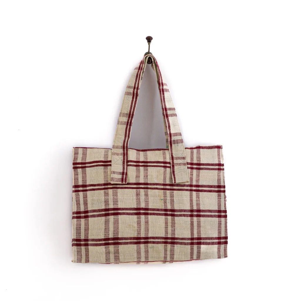 A fabric tote bag with red and beige plaid pattern hangs on a hook against a white background.