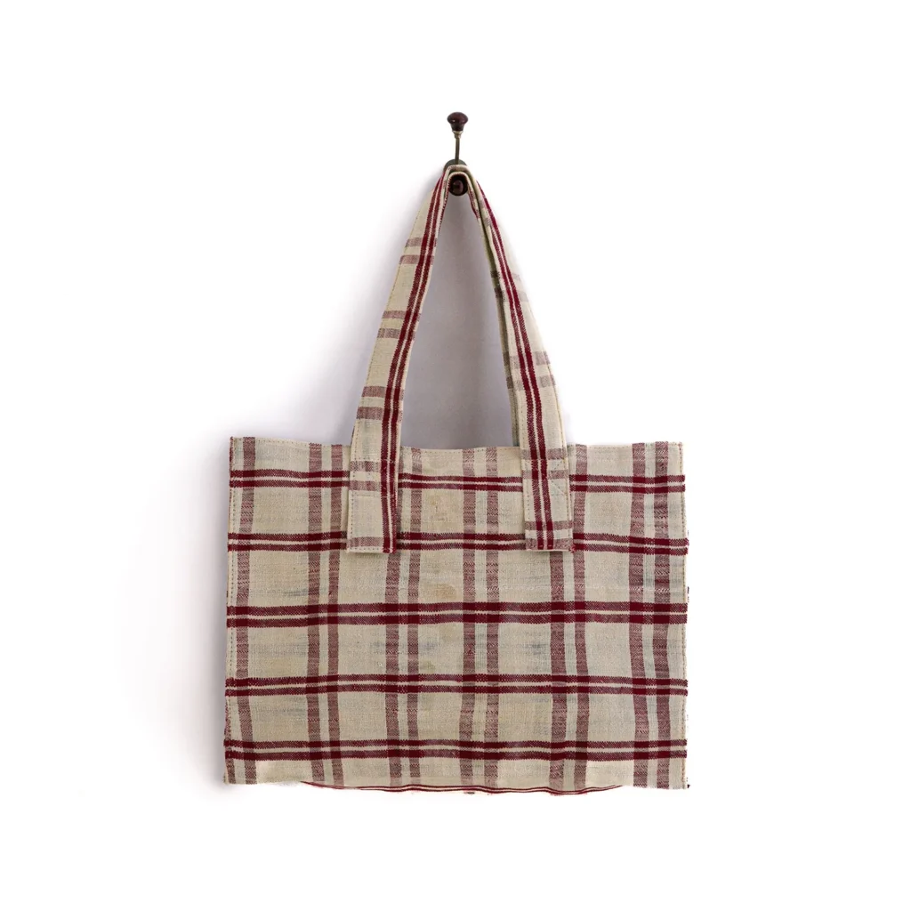 Plaid tote bag with red and beige checks hanging on a hook against a white background.
