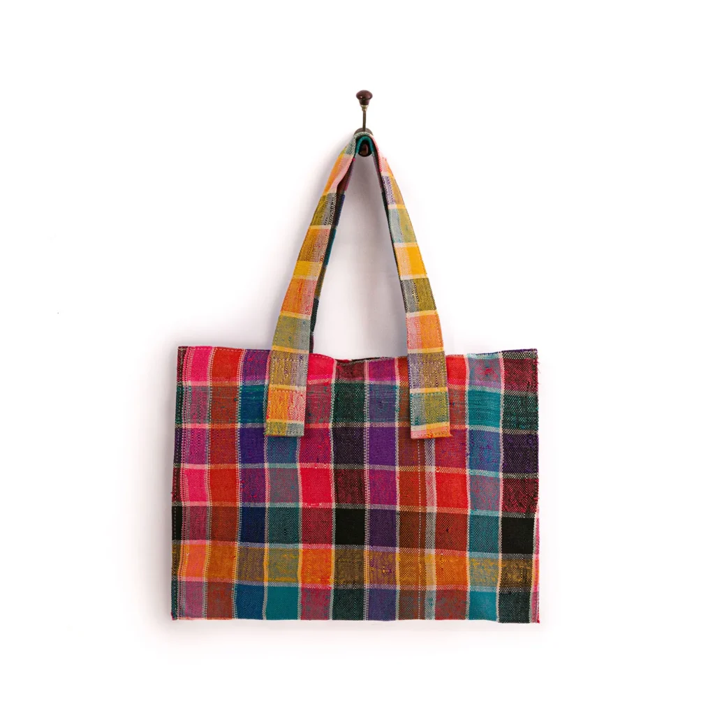 A multicolored checkered tote bag with two handles hangs on a wall hook against a white background.