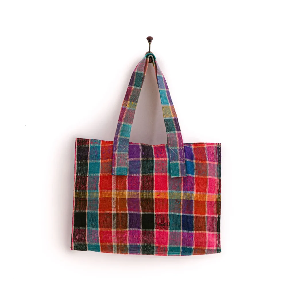 Colorful patchwork tote bag with checkered pattern in various hues, hanging on a wall hook.