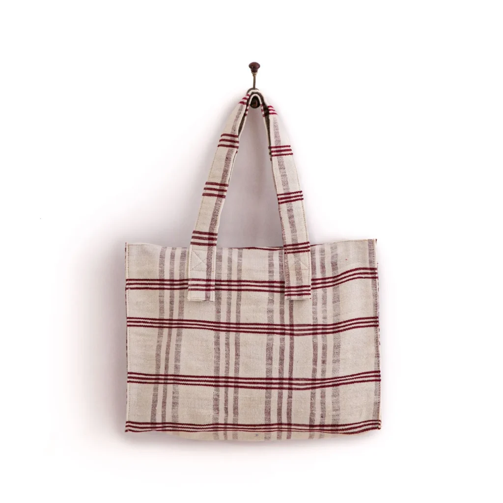 A beige tote bag with red and black stripes hangs on a single metal hook against a white background.