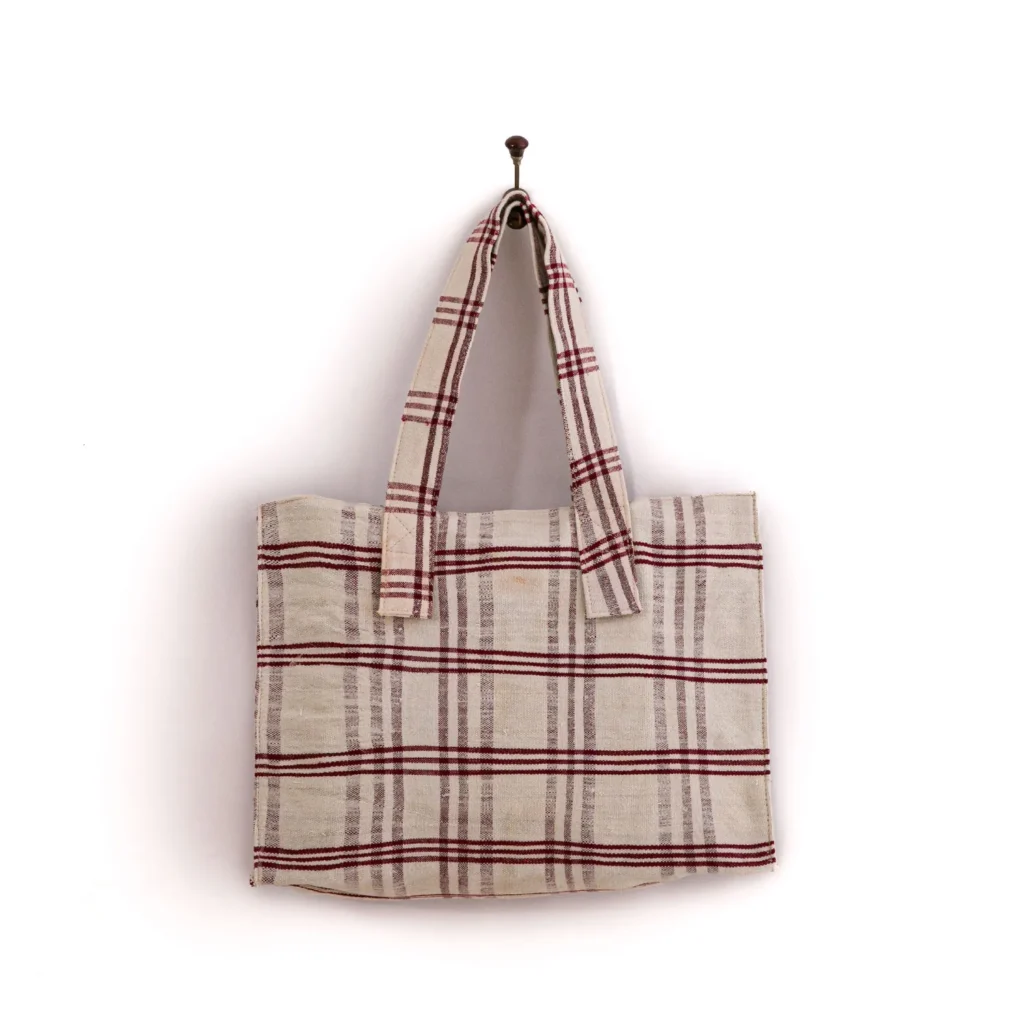 A fabric tote bag with red and white plaid design hangs on a wall hook.