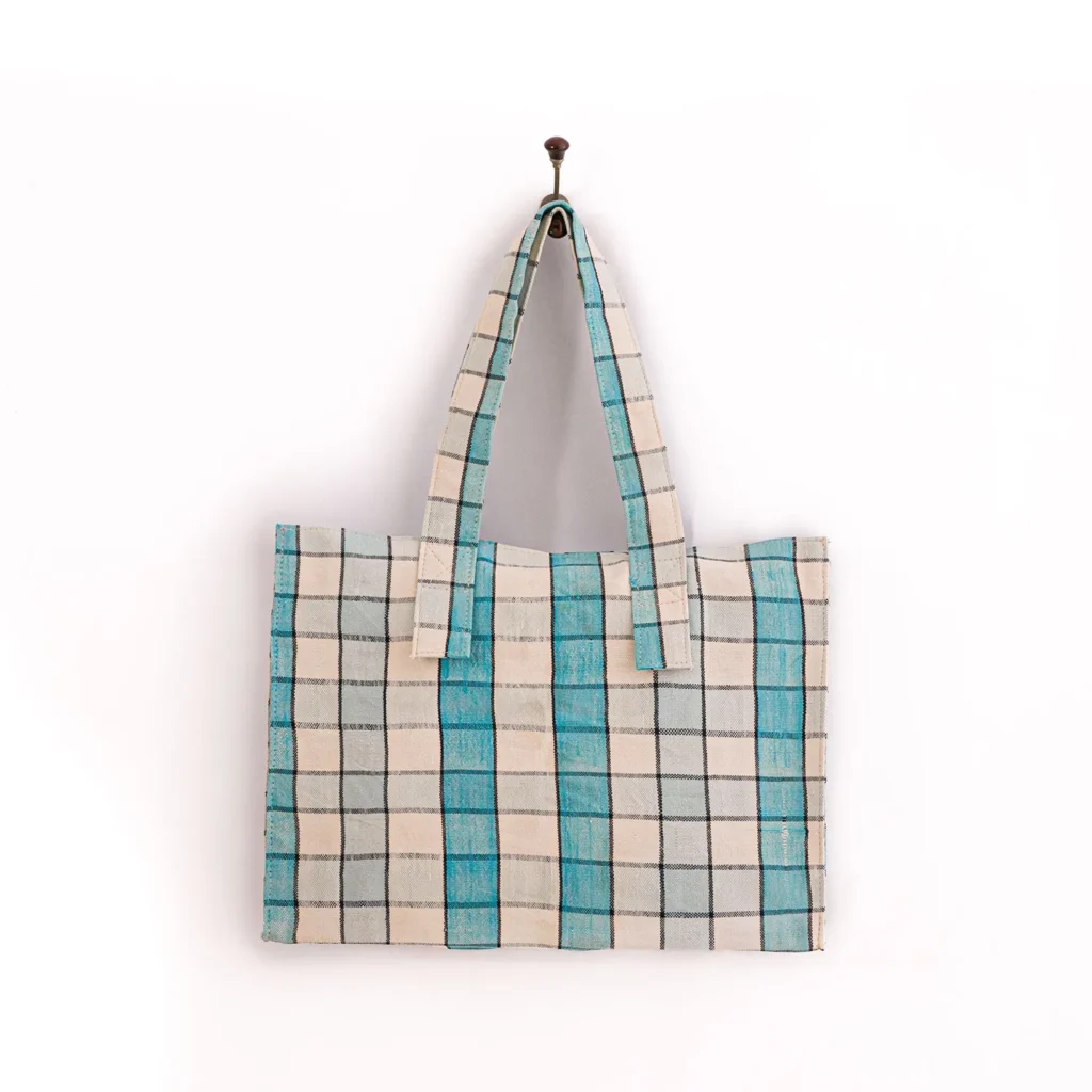 A reusable checkered tote bag with blue and beige patterns hangs on a single hook against a plain white background.