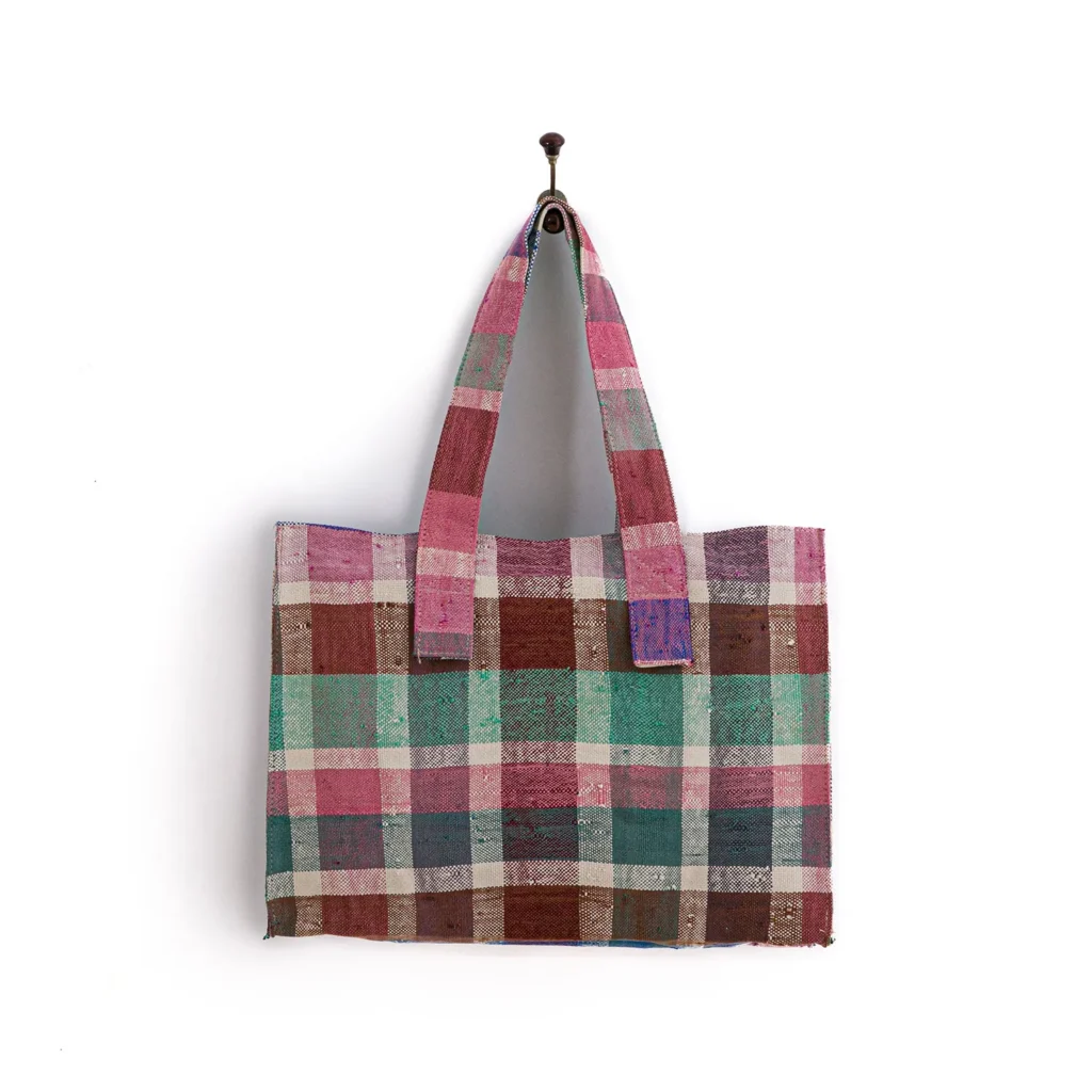 A multicolored checkered tote bag hangs on a hook against a white background.