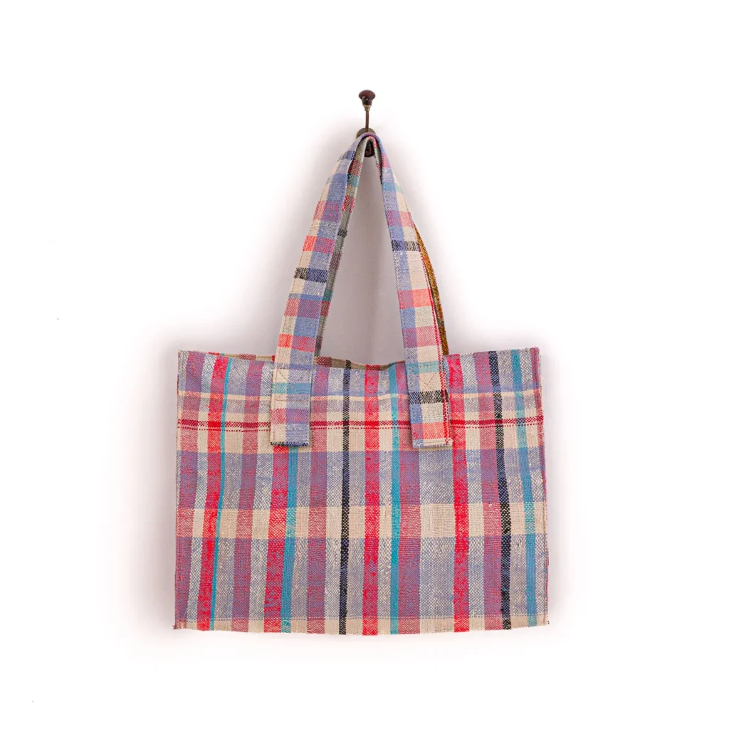 An upcycled weekend bag with a vibrant plaid pattern and two sturdy handles hangs gracefully on a wall hook.