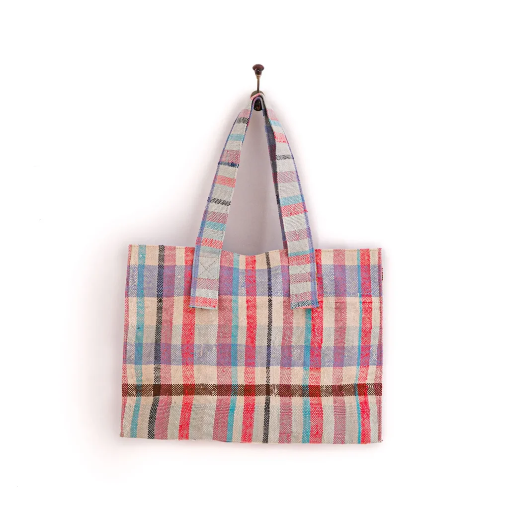An upcycled weekend bag with a multicolored, plaid pattern hangs on a wall hook.