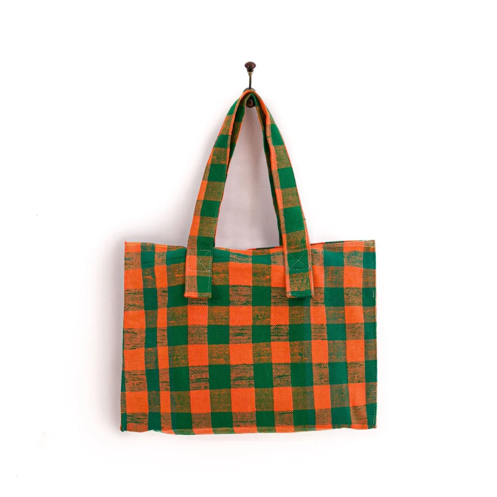 A large, rectangular tote bag with orange and green checkered pattern hangs on a wall hook.