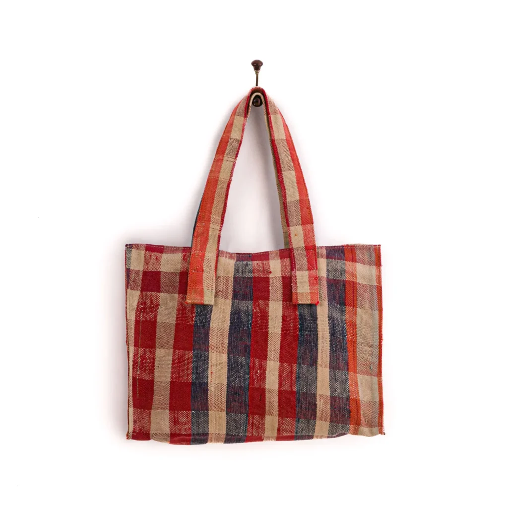 A red, blue, and beige plaid tote bag hangs on a single wall hook against a plain white background.