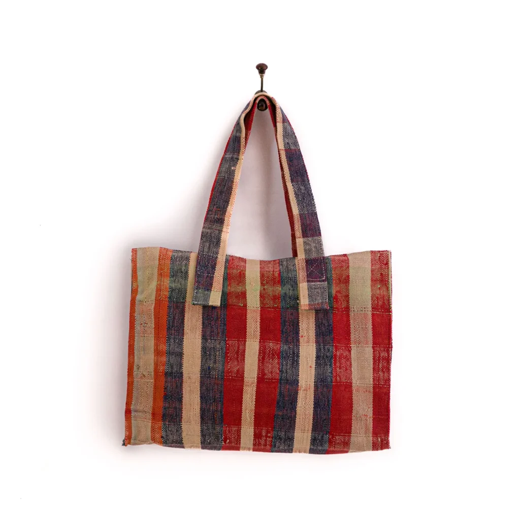 A multicolored striped fabric tote bag hangs on a hook against a plain white background.