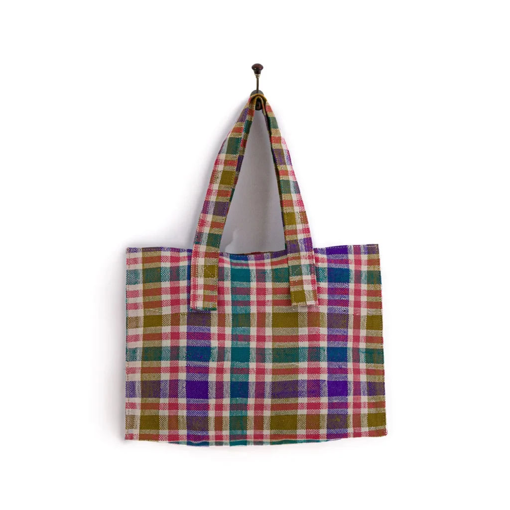 Plaid tote bag with multicolored checkered pattern, hanging on a hook against a plain white background.