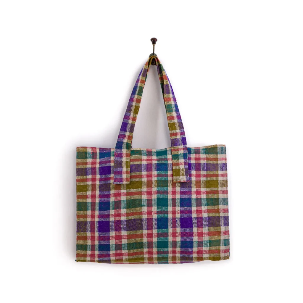 Plaid tote bag with multicolored checkered pattern, hanging on a hook against a plain white background.