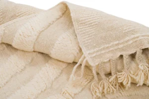 Close-up of a textured, cream-colored woven piece with tassels on one edge, featuring a striped pattern and varied stitching. Perfect for adding a touch of elegance, this design is reminiscent of luxury rugs in its intricate detailing.