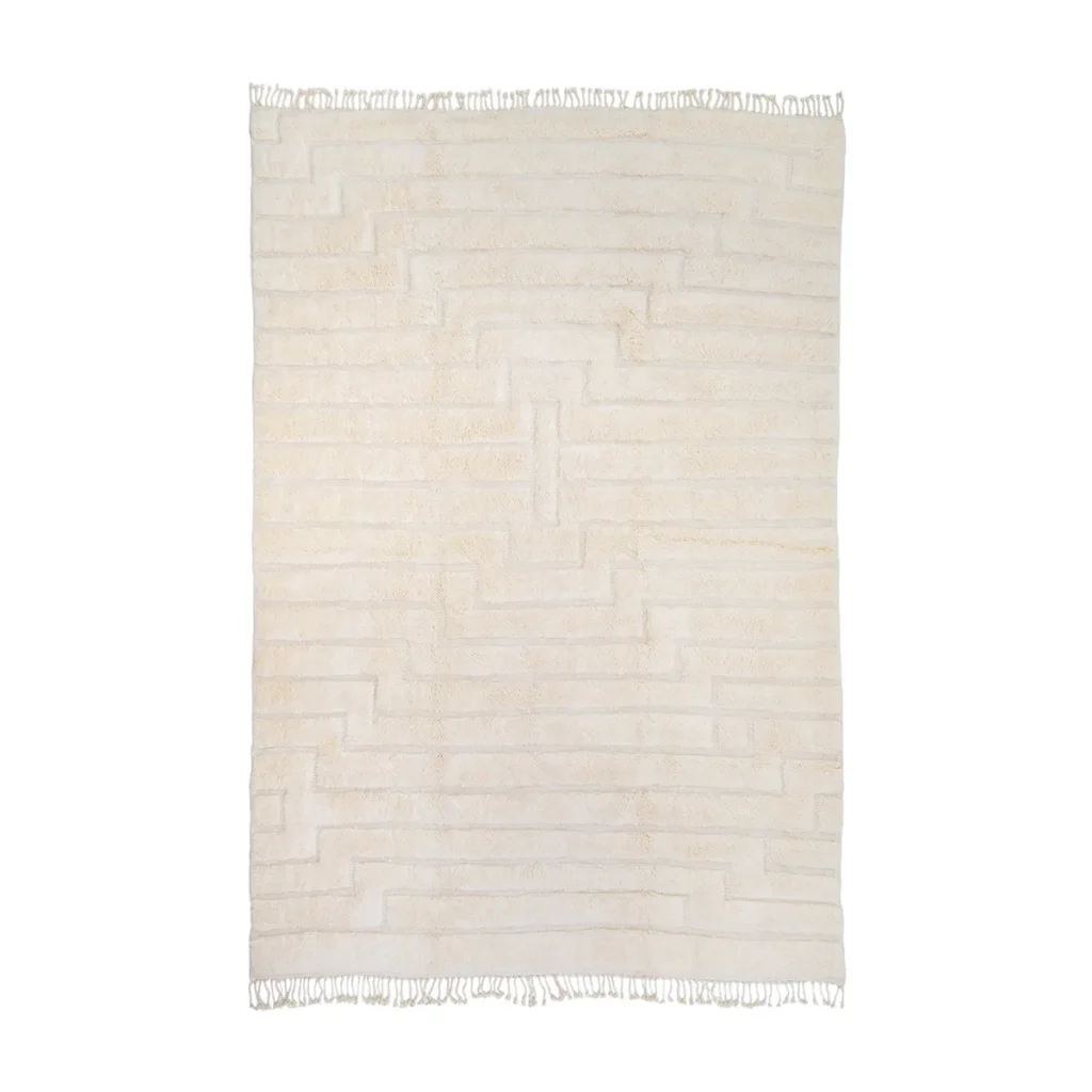 A rectangular, cream-colored rug showcases a striking geometric pattern with fringed edges, adding elegance and style to any room. Perfect for those seeking a touch of sophistication.