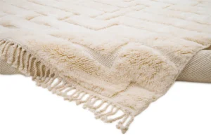 A plush cream-colored throw with a textured geometric pattern and fringe detailing is draped over the edge of a bed, adding a touch of warmth and style.