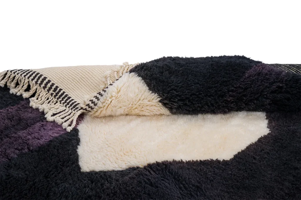 A close-up of a folded, luxurious textile in black, purple, and beige with fringes showcases its soft, fluffy texture.