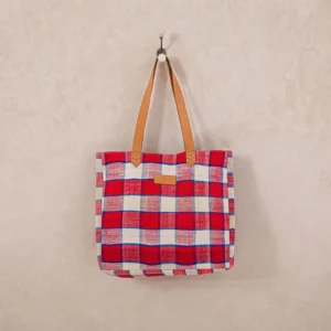 A red and white plaid tote bag with brown leather handles hangs on a wall hook.
