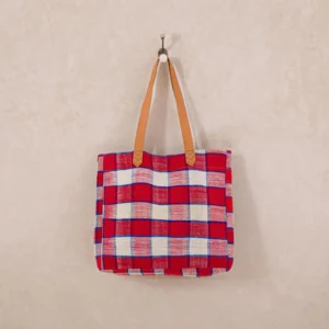 Red and white plaid tote bag with brown handles hanging on a hook against a beige wall.
