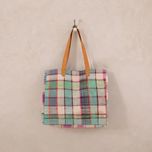 A multicolored plaid tote bag with brown handles hangs on a single wall hook against a beige background.