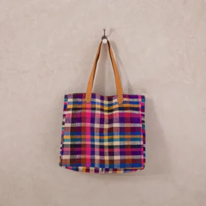 A colorful, plaid-patterned tote bag with leather handles hangs from a wall hook.