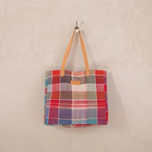A colorful tote bag with plaid patterns in red, blue, and brown hangs on a simple wall hook.
