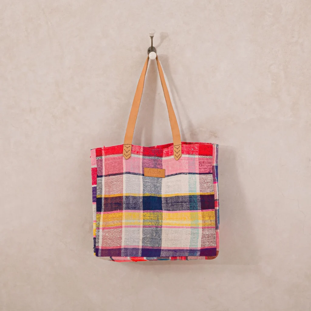 A multicolored plaid tote bag with leather handles hangs on a wall hook.