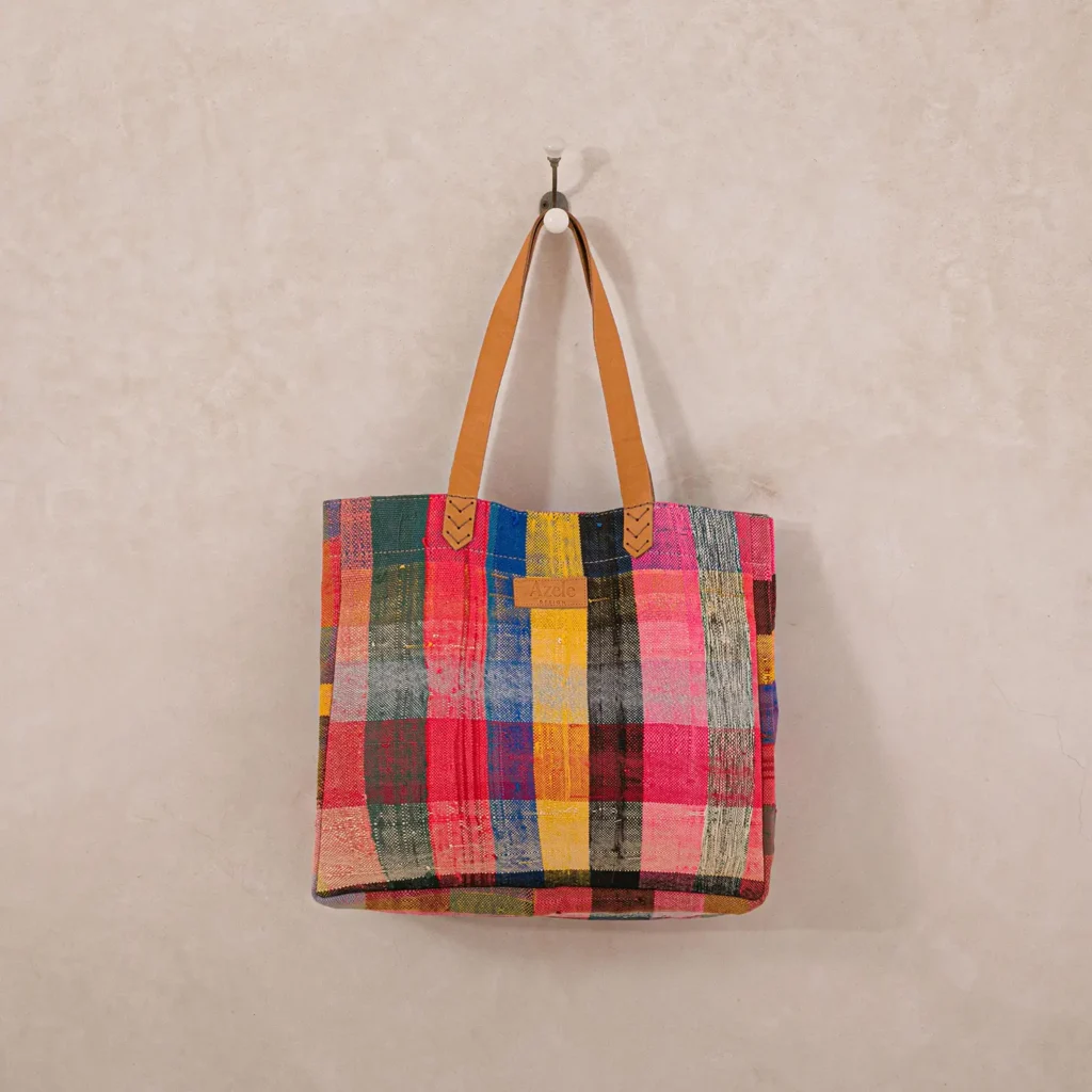 A colorful patchwork tote bag with leather straps hanging on a wall hook.