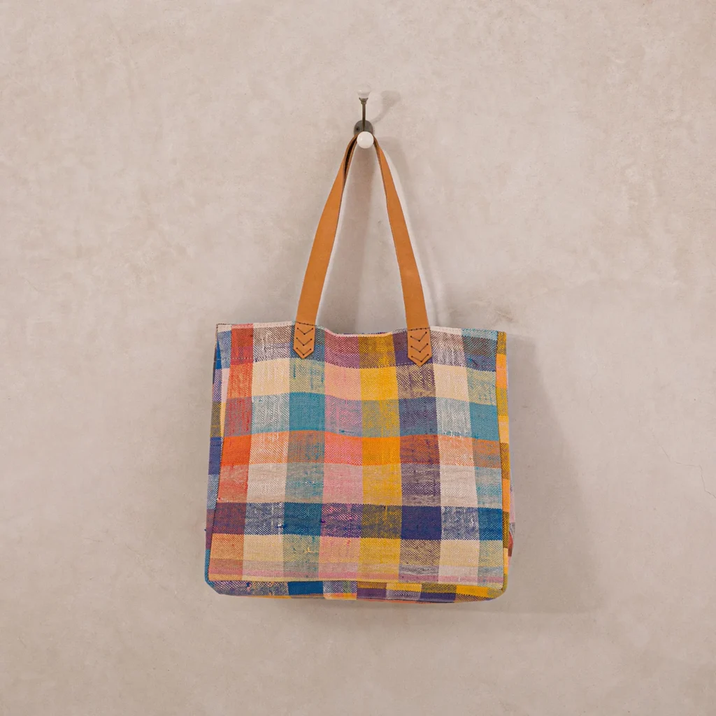 Colorful checkered tote bag with tan handles hanging on a wall hook.
