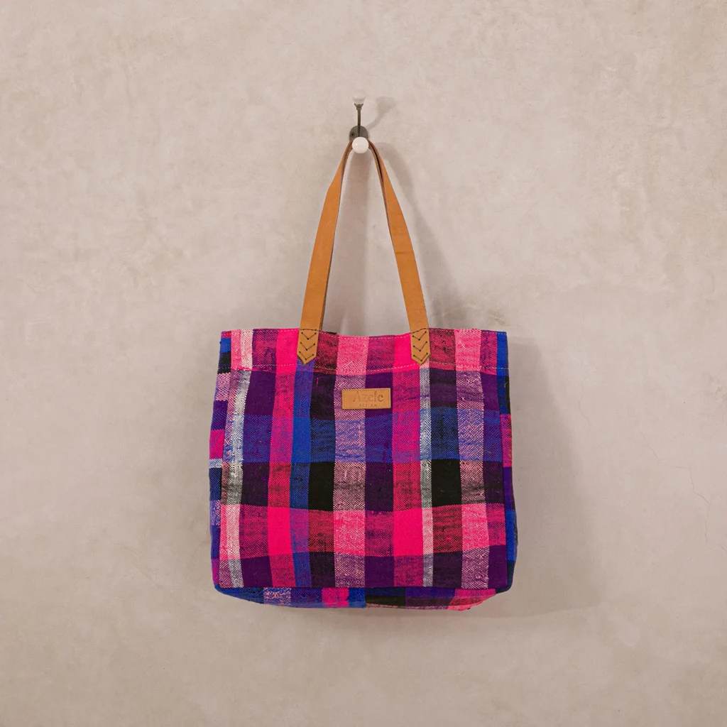 Colorful plaid tote bag with leather handles hangs on a wall hook.