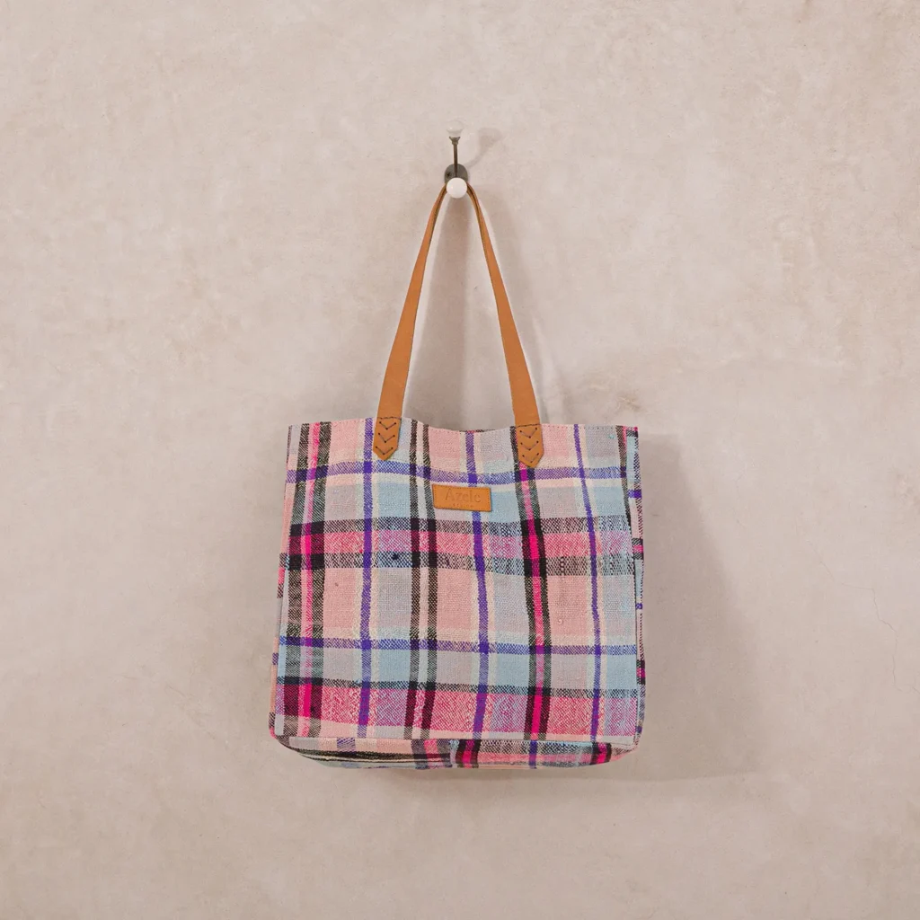 A plaid tote bag with leather handles hangs on a wall hook.