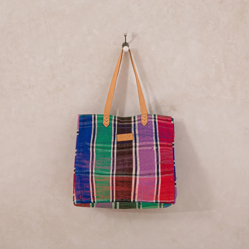 A colorful, plaid-patterned tote bag with leather handles hangs on a wall hook.