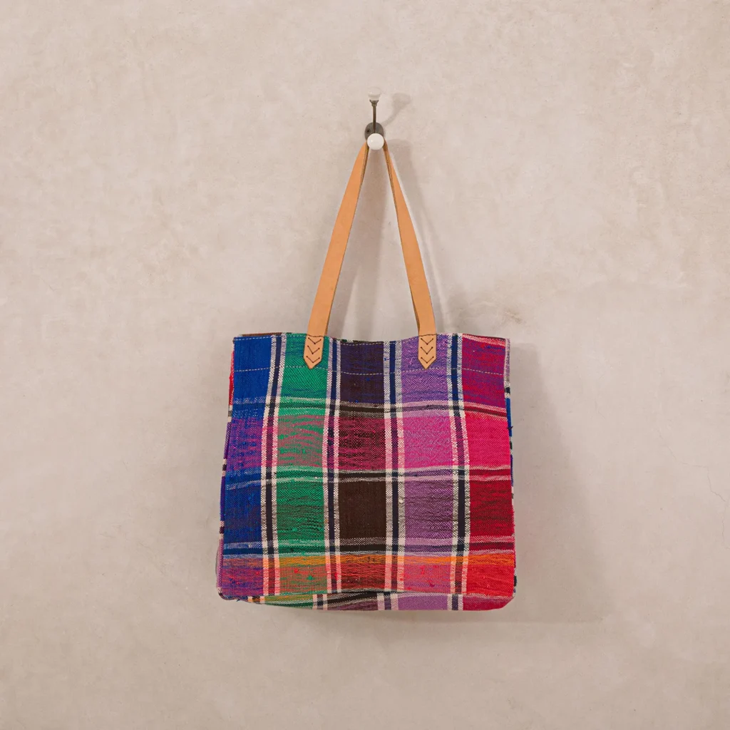 Colorful plaid fabric tote bag with leather handles hanging on a wall hook.