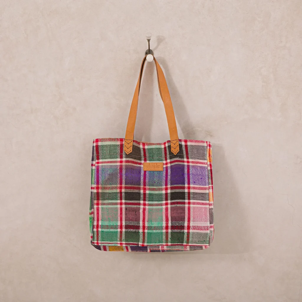 Plaid tote bag with leather handles hanging on a wall hook.