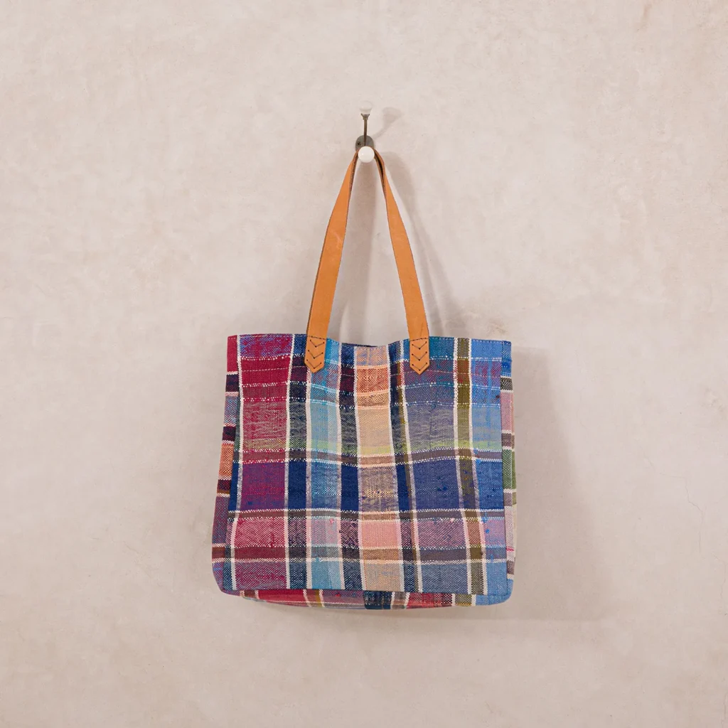 Colorful plaid upcycled shopper bag with brown leather handles hanging on a wall hook.