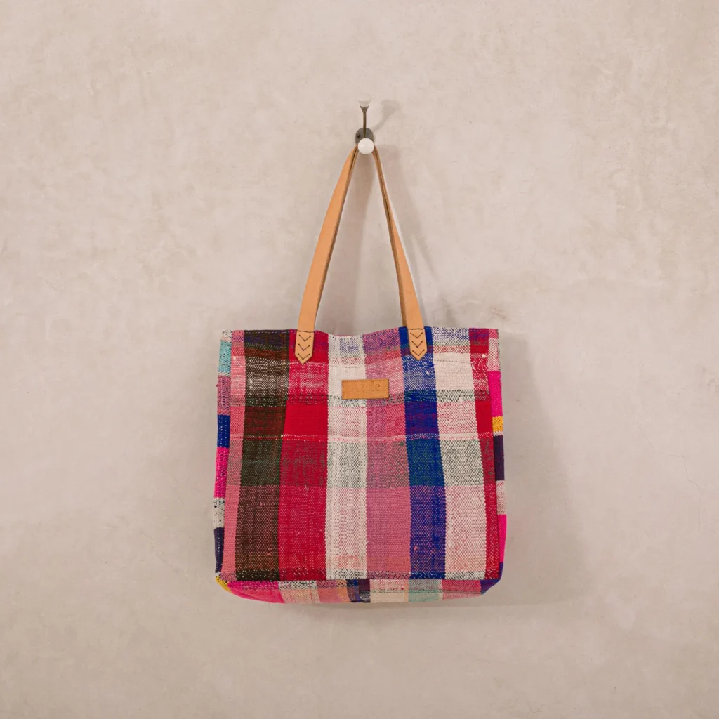 An upcycled shopper bag featuring a plaid pattern and leather handles hangs on a wall hook.