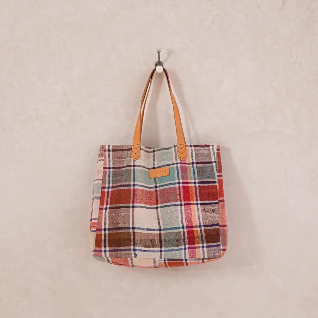 Plaid cloth tote bag with leather handles hanging on a wall hook.