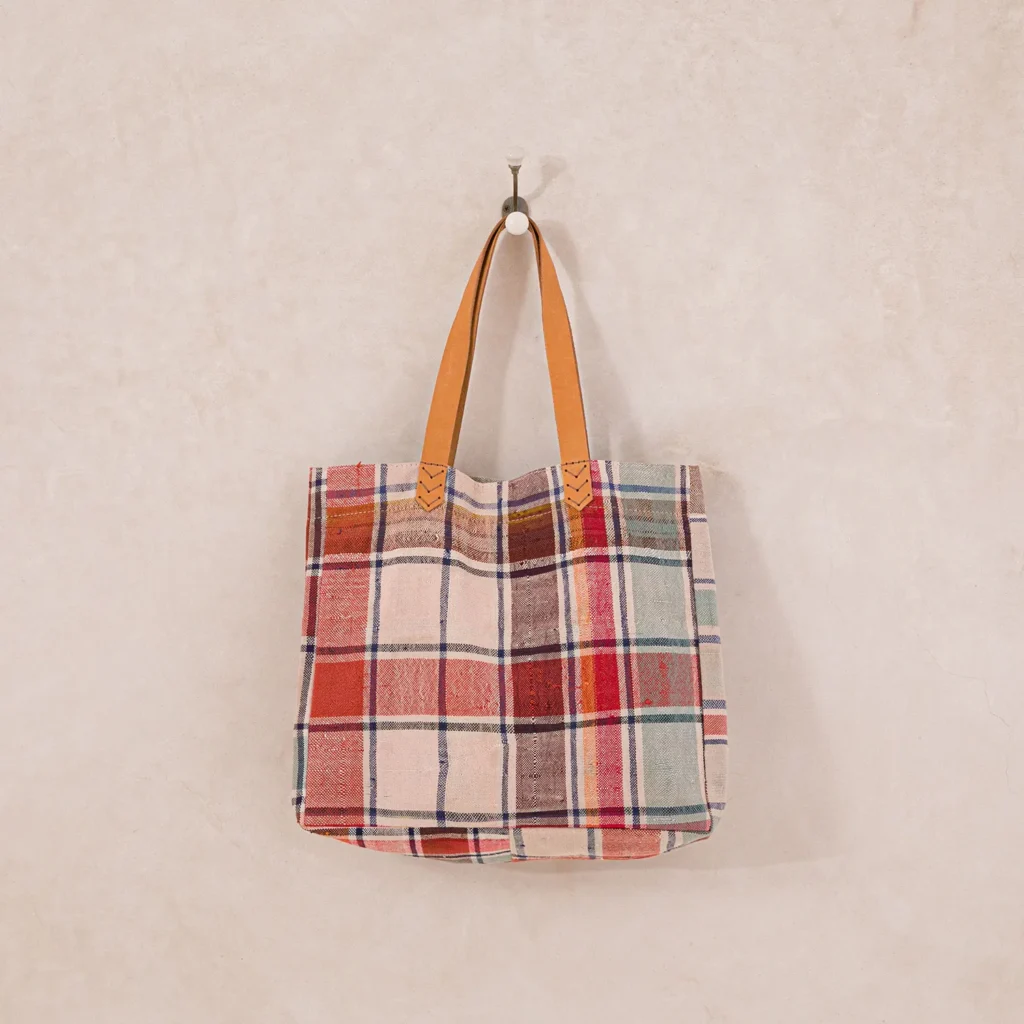 A plaid tote bag with leather handles hangs on a wall hook.