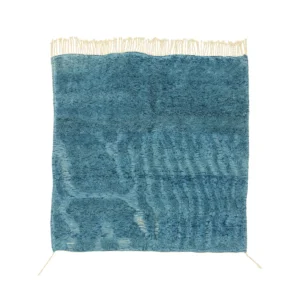 This handmade home decor piece features a blue textured rug with irregular patterns and fringe along the top edge, adding a touch of elegance to any space.