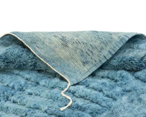 A soft, blue fleece item with a textured pattern is partially folded, revealing a contrasting woven fabric on the reverse side.