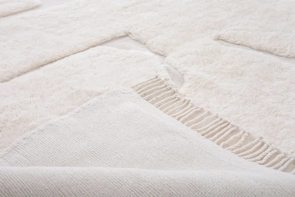 This close-up of a beige textured fabric showcases a woven section with fringe detailing, elegantly creating a pattern of different textures. Perfect for adding a touch of sophistication to any space, this piece embodies the essence of handmade home decor.