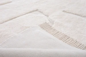 This close-up of a beige textured fabric showcases a woven section with fringe detailing, elegantly creating a pattern of different textures. Perfect for adding a touch of sophistication to any space, this piece embodies the essence of handmade home decor.