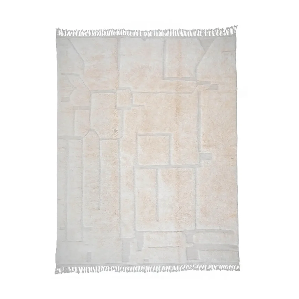 A luxurious beige area rug, hand-knotted with an abstract geometric pattern and fringed edges, adds an elegant touch to any space.