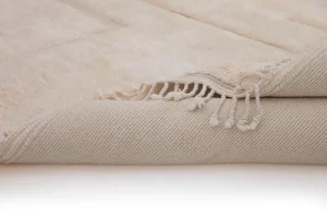 This close-up showcases the intricate details of a luxury rugs corner, elegantly rolled to reveal its textured beige weave and fringe. The hand-knotted pattern and fiber nuances highlight the exquisite craftsmanship typical of handmade home decor.